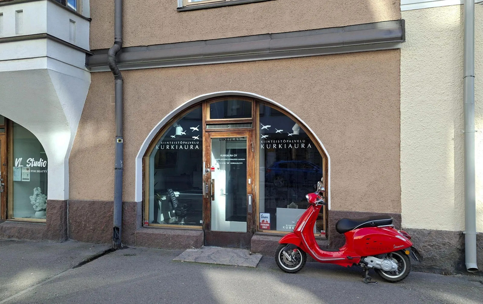 Kurkiauran toimiston kaariovinen sisäänkäynti Pietarinkatu 14:ssä, edessä punainen skootteri.